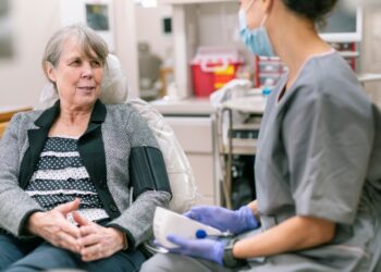 A person sitting in a chair with a nurse in the background Description automatically generated with low confidence